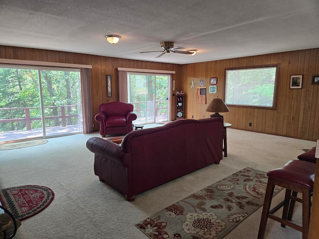 carpeted living room featuring ceiling fan, wooden walls, and a textured ceiling