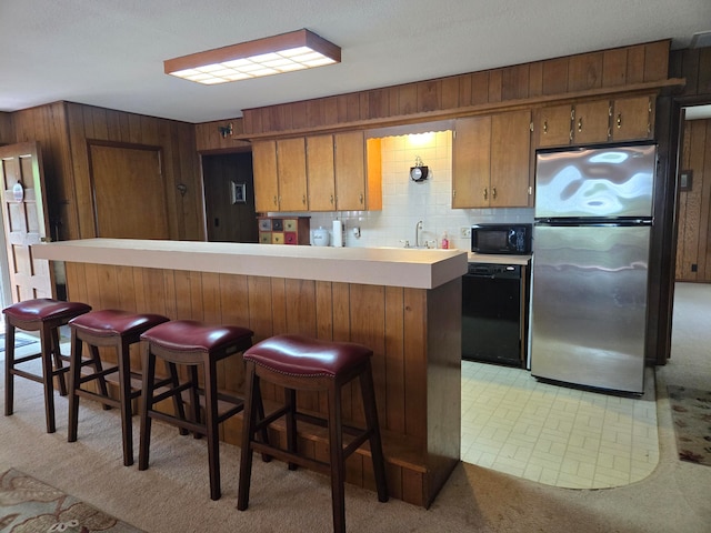 kitchen with tasteful backsplash, a breakfast bar, light carpet, sink, and black appliances