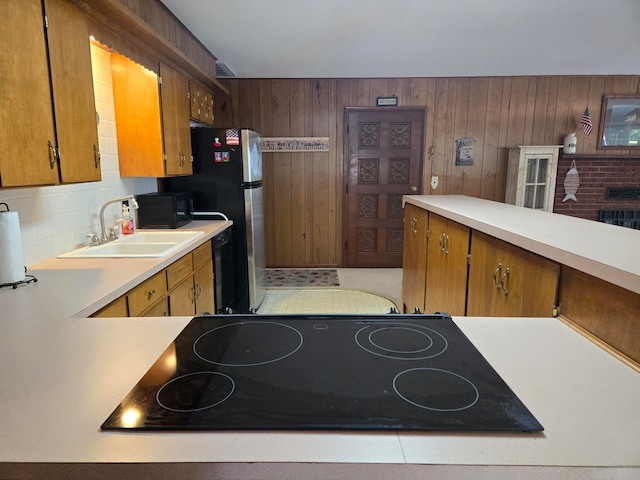 kitchen with black appliances, wood walls, sink, and backsplash