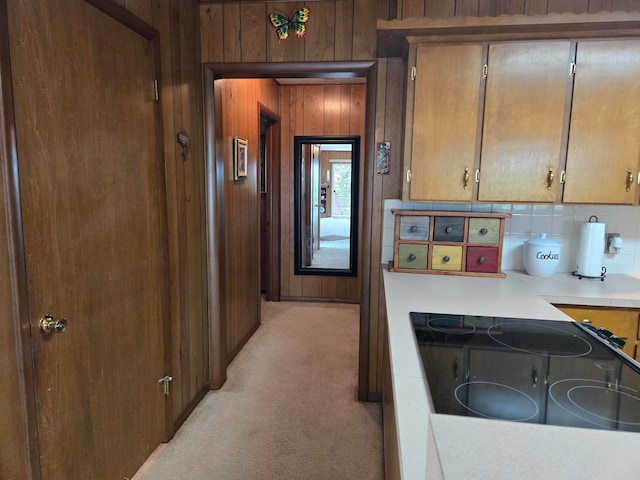 kitchen featuring black stovetop, light colored carpet, wood walls, and tasteful backsplash