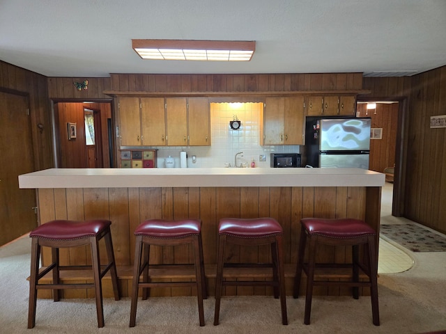 kitchen featuring decorative backsplash, stainless steel refrigerator, wooden walls, and light carpet