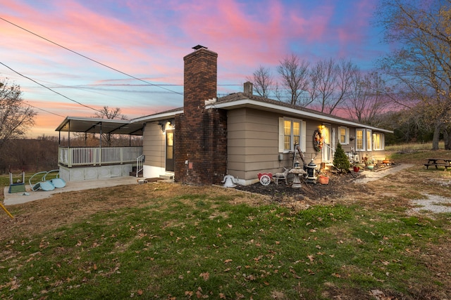 back house at dusk with covered porch and a lawn