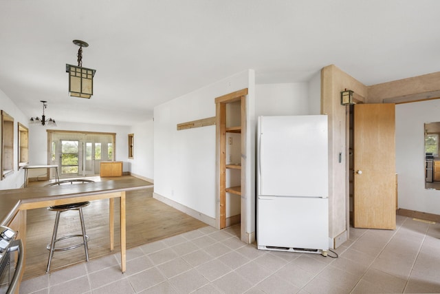 kitchen featuring white refrigerator, hanging light fixtures, stainless steel range, a notable chandelier, and light hardwood / wood-style floors