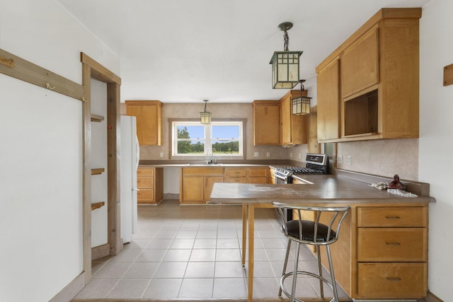 kitchen with stainless steel range with gas stovetop, sink, kitchen peninsula, white refrigerator, and hanging light fixtures