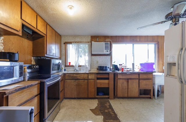 kitchen with a textured ceiling, appliances with stainless steel finishes, a wall mounted air conditioner, and a wealth of natural light