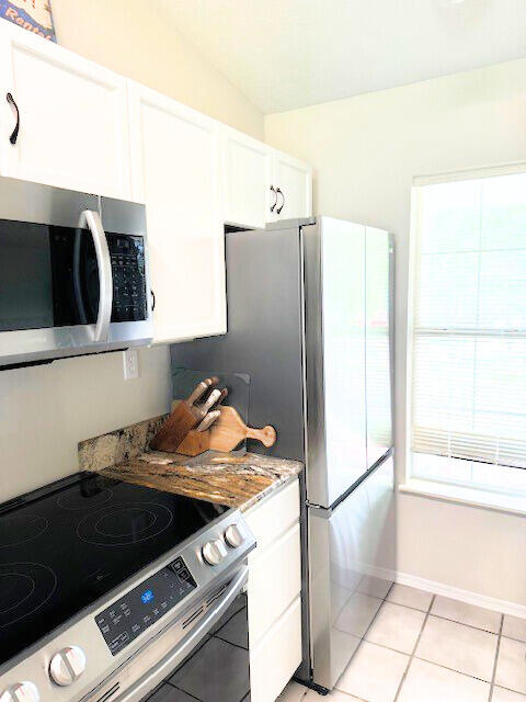 kitchen with light stone counters, lofted ceiling, light tile patterned floors, range with electric cooktop, and white cabinetry