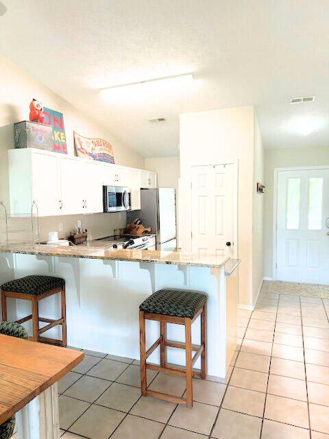 kitchen with lofted ceiling, kitchen peninsula, white cabinetry, refrigerator, and a breakfast bar area