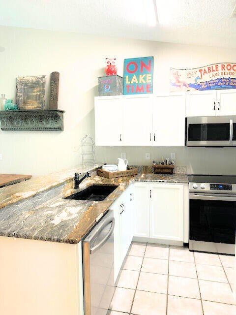 kitchen featuring light tile patterned floors, sink, white cabinetry, appliances with stainless steel finishes, and dark stone countertops