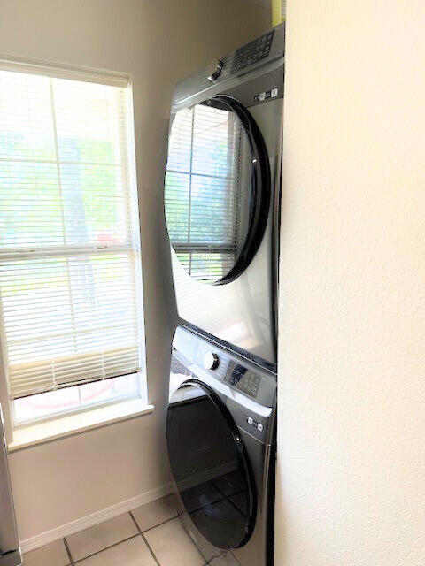 laundry area with stacked washer and dryer, a wealth of natural light, and light tile patterned floors