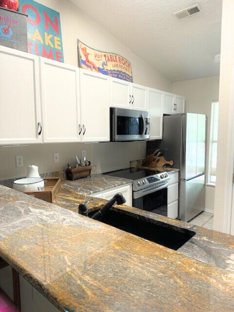 kitchen with white cabinets, sink, light tile patterned flooring, vaulted ceiling, and appliances with stainless steel finishes