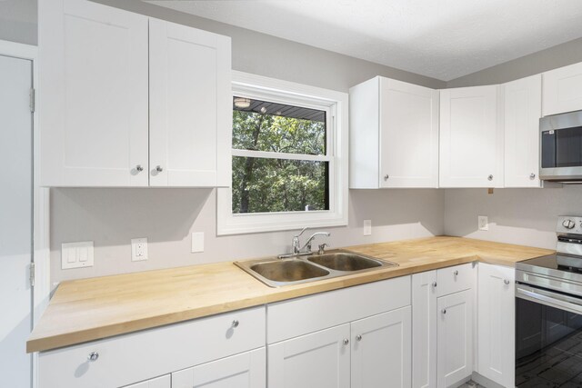 kitchen featuring stainless steel appliances, a textured ceiling, butcher block countertops, sink, and white cabinetry