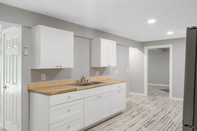 kitchen with sink, stainless steel fridge, white cabinets, and butcher block counters