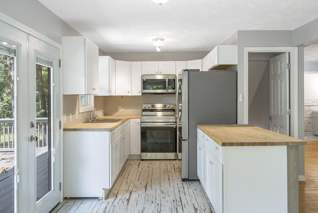 kitchen with stainless steel appliances, sink, white cabinets, a textured ceiling, and butcher block countertops