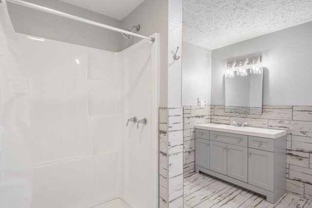 bathroom with tile walls, walk in shower, vanity, and a textured ceiling