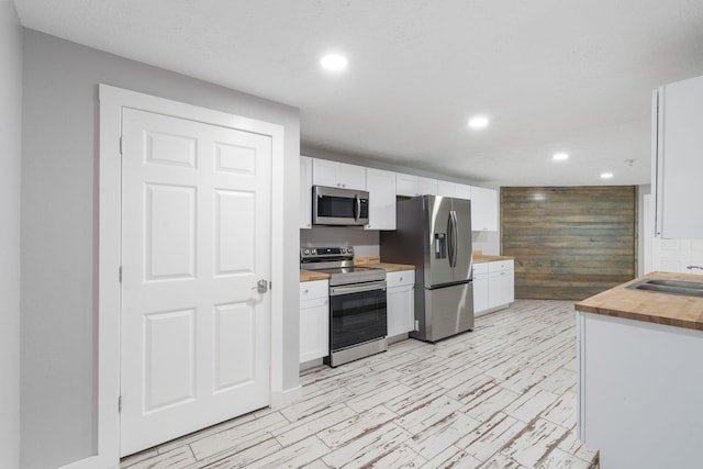 kitchen featuring wood walls, butcher block countertops, white cabinets, appliances with stainless steel finishes, and sink