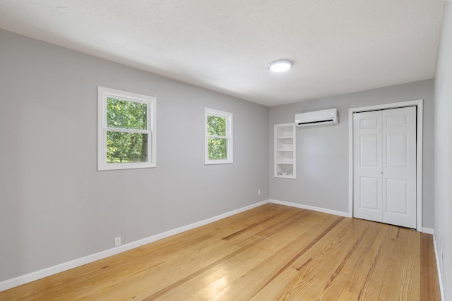 unfurnished bedroom with a textured ceiling, hardwood / wood-style flooring, and a wall mounted air conditioner