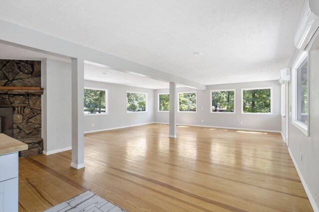 unfurnished living room featuring plenty of natural light, light wood-type flooring, a wall mounted air conditioner, and a stone fireplace