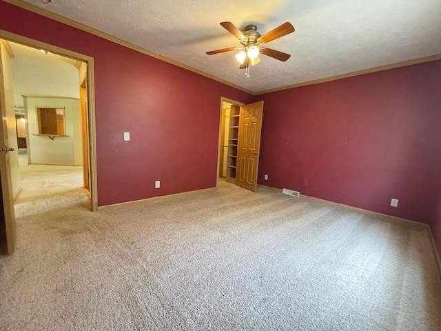 carpeted spare room with a textured ceiling, a ceiling fan, baseboards, and ornamental molding