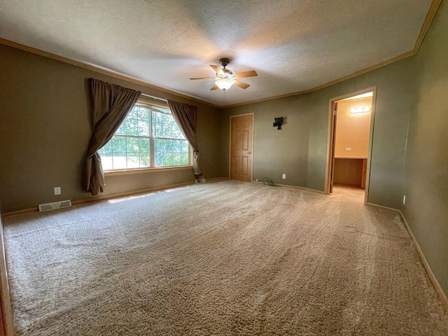 carpeted empty room with a ceiling fan, crown molding, a textured ceiling, baseboards, and visible vents