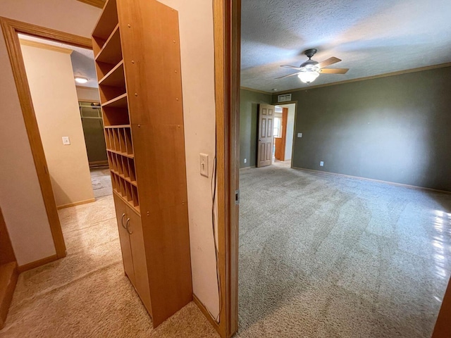 hall with light carpet, a textured ceiling, and ornamental molding