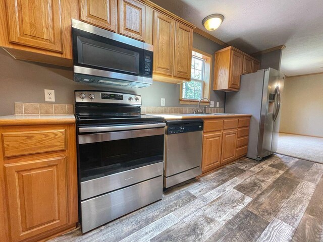 kitchen with ornamental molding, light wood-style flooring, stainless steel appliances, and a sink