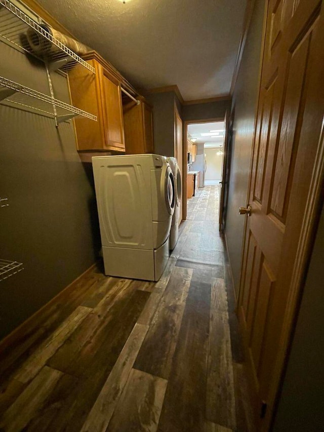 clothes washing area with crown molding, washing machine and clothes dryer, cabinets, and dark hardwood / wood-style flooring