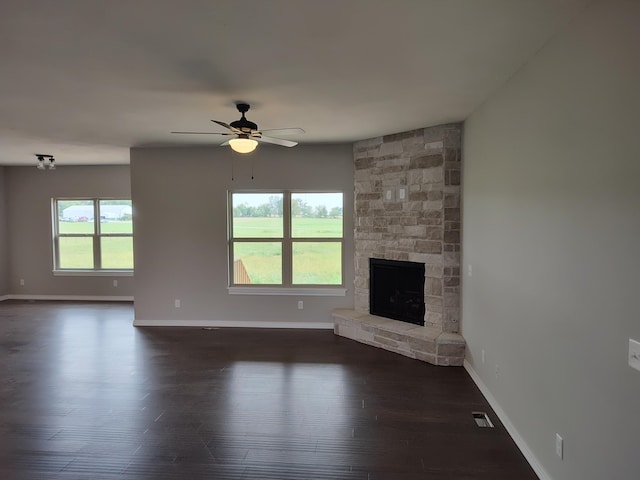 unfurnished living room featuring a stone fireplace, a wealth of natural light, ceiling fan, and dark wood-type flooring