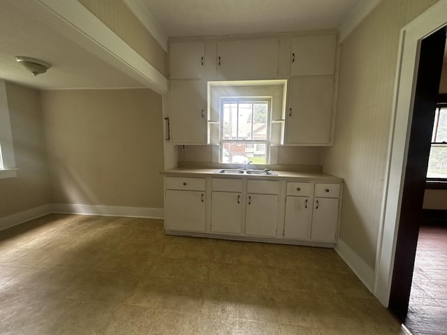 kitchen featuring white cabinets, baseboards, a sink, and light countertops