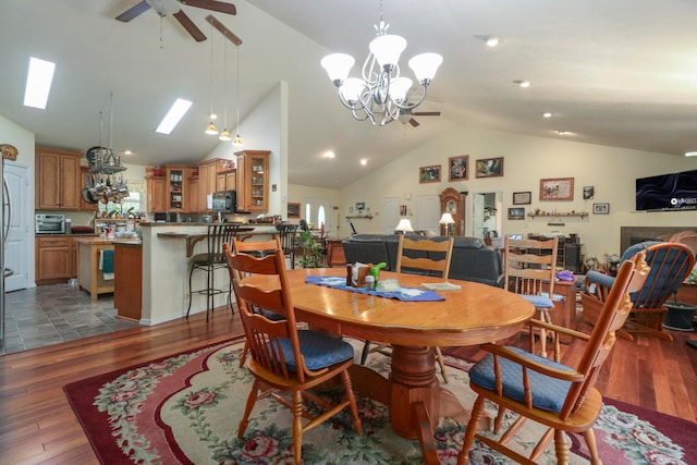 dining area featuring ceiling fan with notable chandelier, dark wood-type flooring, and vaulted ceiling with skylight