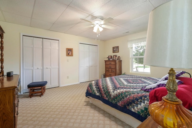 carpeted bedroom featuring a paneled ceiling, ceiling fan, and two closets