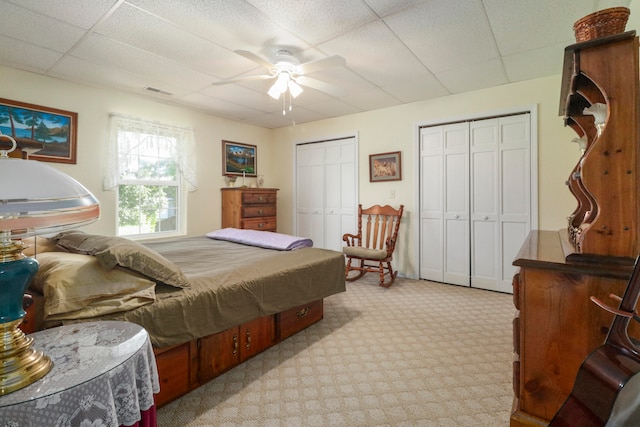 bedroom featuring light carpet, a paneled ceiling, ceiling fan, and multiple closets