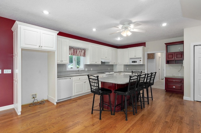 kitchen with a center island, wood-type flooring, white appliances, white cabinetry, and a kitchen breakfast bar