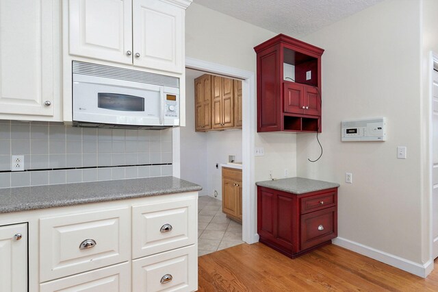 kitchen featuring white cabinets, a textured ceiling, light wood-type flooring, and backsplash