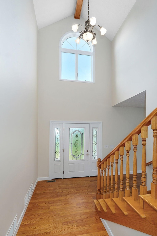 foyer entrance featuring beam ceiling, high vaulted ceiling, a wealth of natural light, and light hardwood / wood-style flooring