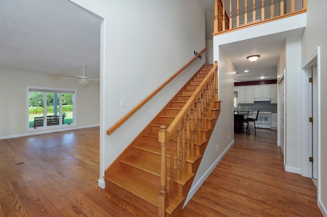 staircase with hardwood / wood-style flooring, ceiling fan, and a textured ceiling