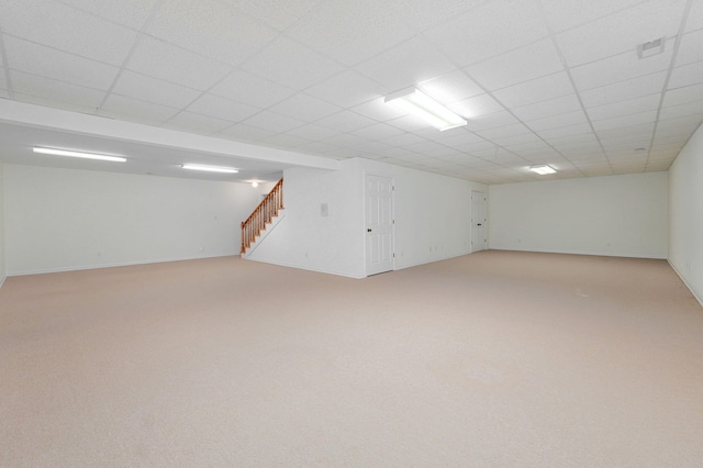 basement featuring a paneled ceiling and light carpet