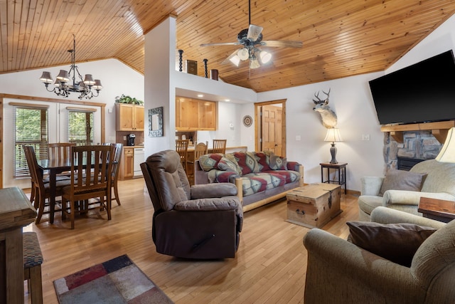 living room with ceiling fan with notable chandelier, high vaulted ceiling, light wood-type flooring, and a stone fireplace