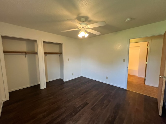 unfurnished bedroom with a textured ceiling, ceiling fan, two closets, and dark hardwood / wood-style flooring