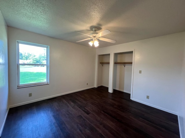 unfurnished bedroom featuring a textured ceiling, ceiling fan, multiple closets, and dark hardwood / wood-style flooring