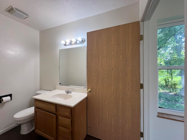 bathroom with vanity, toilet, a textured ceiling, and a healthy amount of sunlight