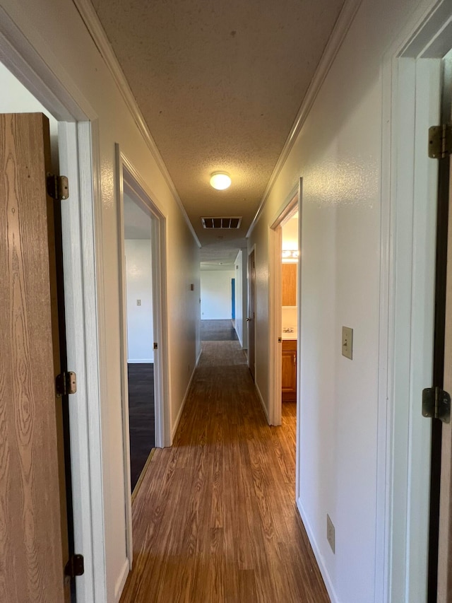 hall with wood-type flooring, ornamental molding, and a textured ceiling