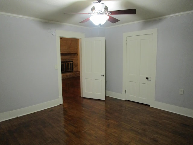 spare room with ceiling fan, dark hardwood / wood-style flooring, ornamental molding, and a brick fireplace