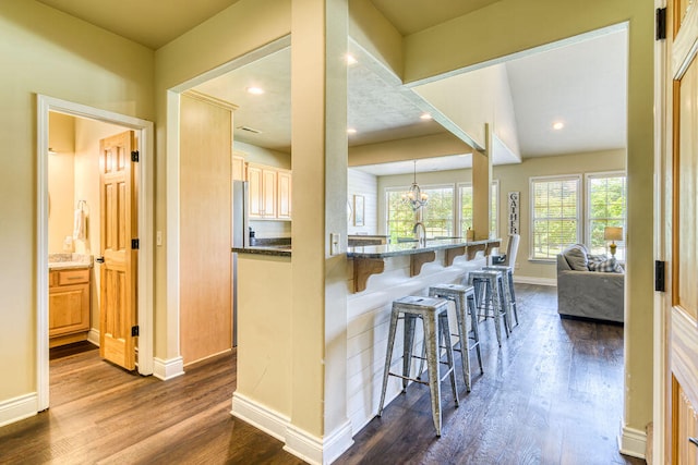 kitchen with hanging light fixtures, stainless steel refrigerator, dark hardwood / wood-style floors, dark stone countertops, and a breakfast bar area