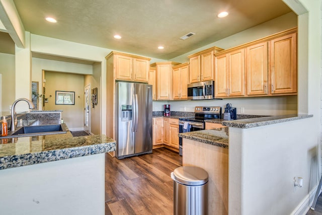 kitchen with stainless steel appliances, light brown cabinets, dark stone countertops, dark wood-type flooring, and sink