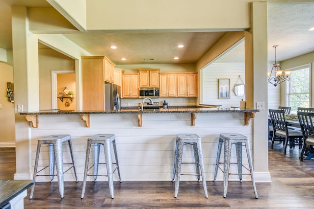 kitchen featuring pendant lighting, stainless steel appliances, a breakfast bar area, dark stone counters, and dark hardwood / wood-style flooring