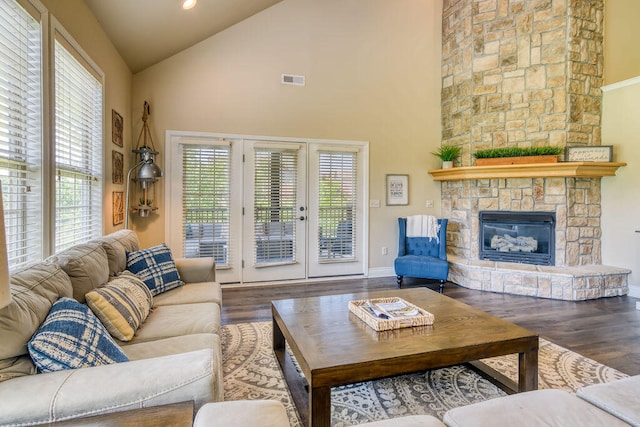 living room with a stone fireplace, dark wood-type flooring, and high vaulted ceiling