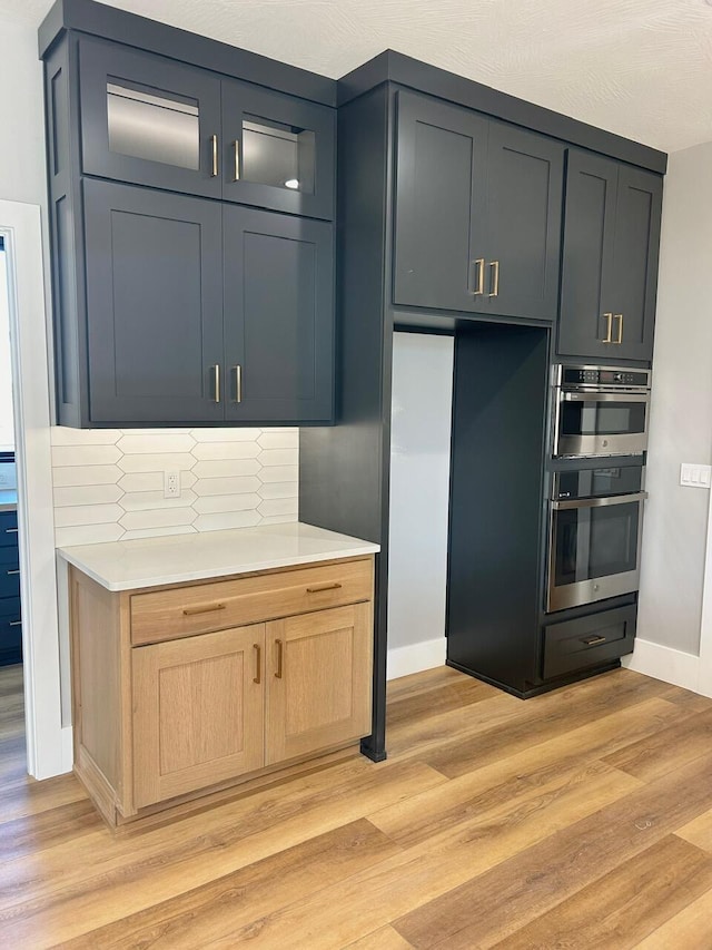 kitchen featuring decorative backsplash, light brown cabinets, light wood-type flooring, and double oven