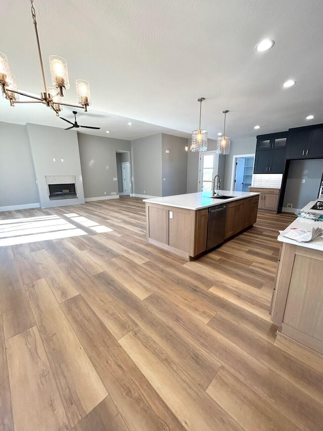 kitchen featuring sink, dishwasher, pendant lighting, wood-type flooring, and a kitchen island with sink