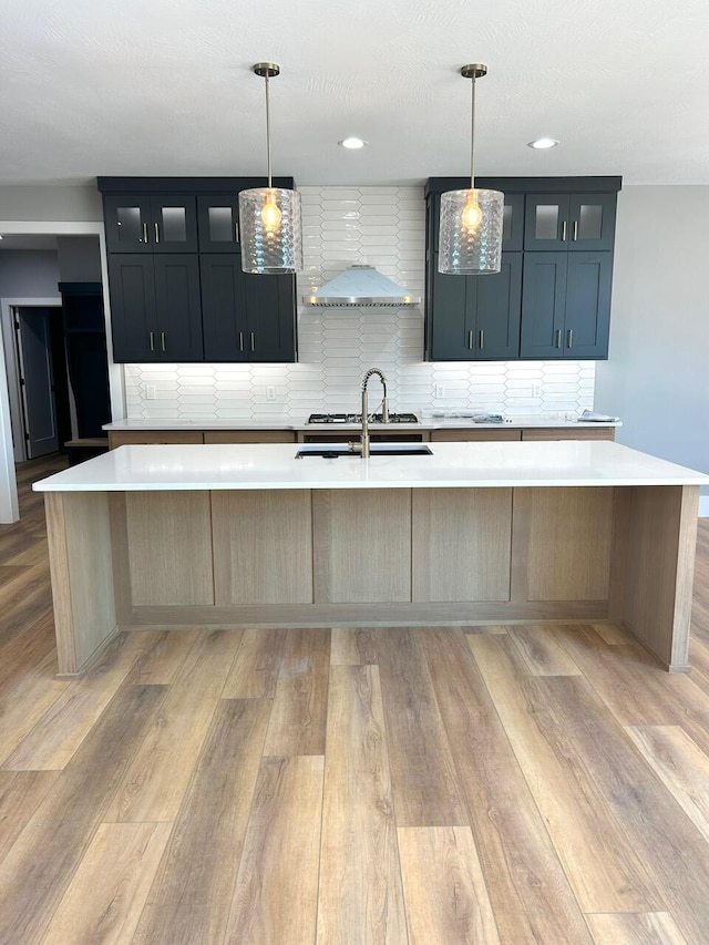 kitchen featuring decorative light fixtures, backsplash, and a large island with sink