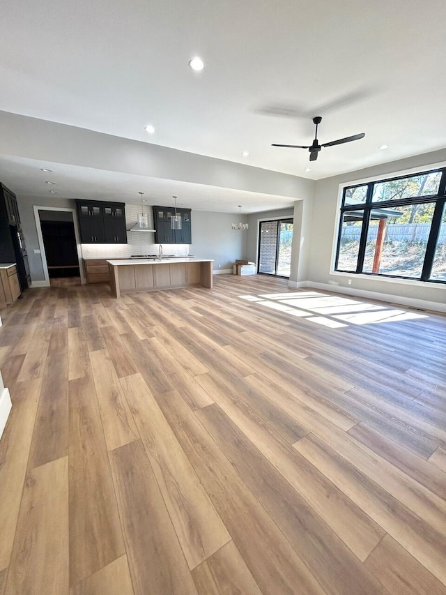 unfurnished living room with ceiling fan with notable chandelier and light hardwood / wood-style flooring